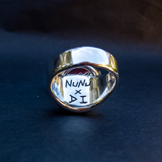 The underside of a polished sterling silver signet ring. The ring is carved with the words "Nunu x DI"