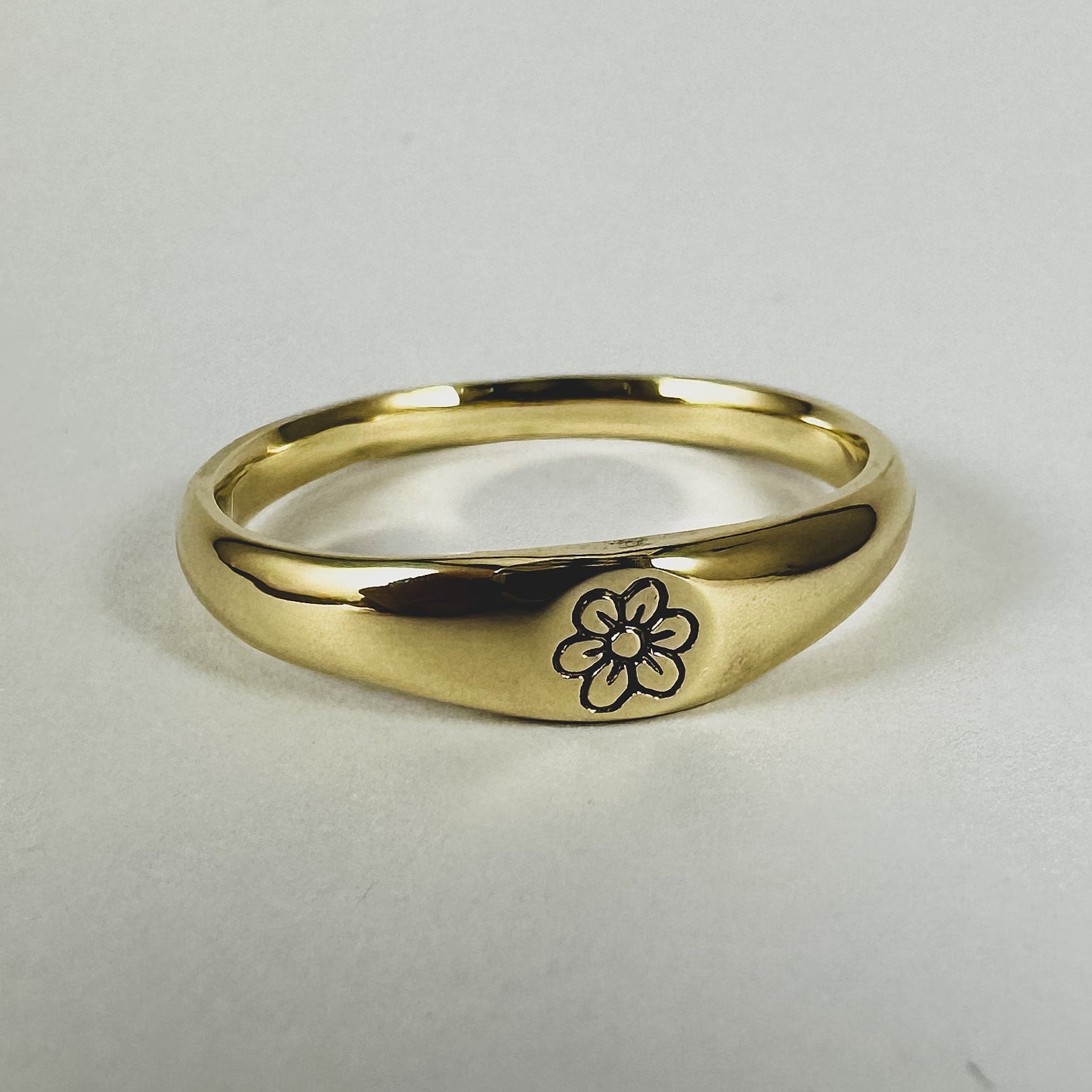 A solid 9ct yellow gold band ring with a hand-carved flower design on it, displayed against a white background.