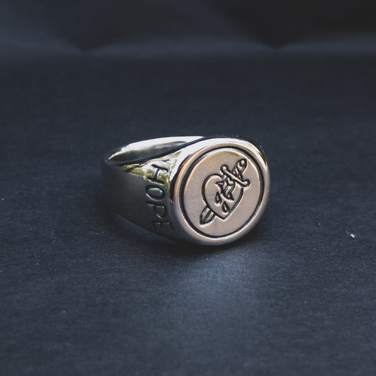 A sterling silver signet ring with a polished finish, featuring a graphic of a heart with a knife through it. The ring is carved with the word "hopeless".